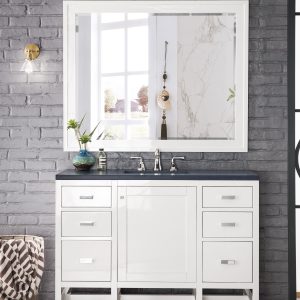 A modern bathroom features the Addison 48 inch Bathroom Vanity in Glossy White with a dark countertop and silver faucets. A large rectangular mirror is mounted on the gray brick wall, accented by a small plant and decor items. Natural light streams through a window, brightening the serene space.
