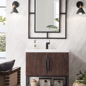 A modern bathroom showcases the Columbia 31.5 Vanity in Coffee Oak with a white countertop beneath a geometric black-framed mirror. Flanked by two wall-mounted lamps, baskets rest on a shelf under the sink, while a potted plant blooms near the window.