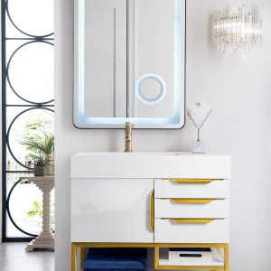 A modern bathroom showcases the Columbia 36 Single Bathroom Vanity in Glossy White and Radiant Gold, with a backlit rectangular mirror above. It includes three drawers, a shelf with blue towels, and a pristine tray. A stylish wall sconce is on the right; circular window patterns adorn the left.