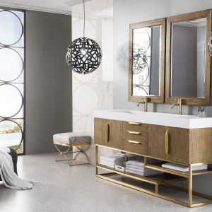 In a modern bathroom, the Columbia 72 Double Bathroom Vanity in Latte Oak with Radiant Gold features prominently, topped by large mirrors. Spherical lamps provide lighting while a wicker chair with a towel invites relaxation. Expansive windows flood the space with natural light.