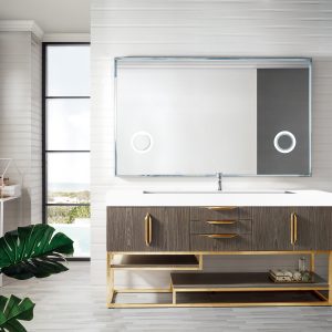The Columbia 72 Single Bathroom Vanity in Ash Gray features a large mirror with radiant gold accents. It includes drawers and open shelves, with modern decor pieces adorning the top. A potted plant adds freshness, while tall windows bring in natural light.