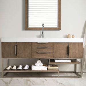 The Columbia 72 Single Bathroom Vanity in Latte Oak and Brushed Nickel includes a spacious wooden cabinet, three central drawers, and two side doors. Below are shelves with neatly stacked towels, slippers, decor items; a robe hangs on the right, with an elegant framed mirror above the sink.
