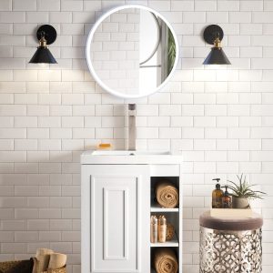 A modern bathroom features the Alicante 24 Bathroom Vanity in glossy white with an illuminated round mirror above. Open shelves store towels and toiletries. Two wall sconces flank the mirror, and a decorative side table holds soap and a plant.