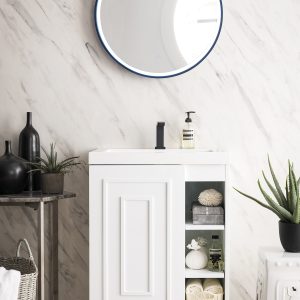 A contemporary bathroom features the Alicante 24 Bathroom Vanity in glossy white with matte black fixtures, topped by a circular mirror. Open shelves organize towels and toiletries, a potted plant on the right, and a decorative black vase adorns the left table.
