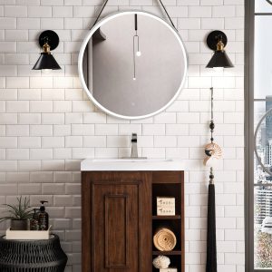 Modern bathroom with white subway tiles and an Alicante 24 Bathroom Vanity in Mid Century Acacia. A round mirror with a hanging strap complements the black wall sconces. A cityscape is visible through the tall window, while decorative items adorn the vanity and nearby stool.