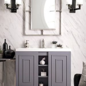 A modern bathroom features the Alicante 39.5 Bathroom Vanity in Grey Smoke with a marble backsplash, white countertop, and brushed nickel fixtures. A square mirror is framed by sleek sconces, while decorative items sit on the vanitys open shelf and nearby table.