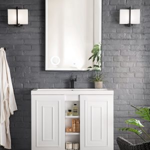 The bathroom boasts an Alicante 39.5 Bathroom Vanity in glossy white and matte black, set against a dark gray brick wall. A mirror with flanking wall lights enhances the space, while open shelves showcase toiletries. A towel hook and plants add warmth and greenery.