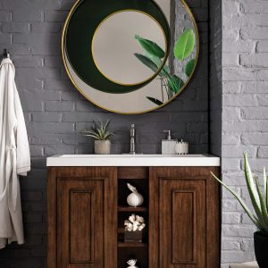 The Alicante 39.5 Bathroom Vanity in Mid Century Acacia features a white countertop under a large circular mirror reflecting lush greenery. Gray brick walls enhance the wooden textures, with a robe nearby and an aloe plant elegantly placed on the floor.
