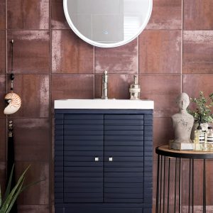 A modern bathroom highlights a circular mirror above a Navy Blue Linden 24 inch Bathroom Vanity with vertical slats. The textured brown tile wall contrasts with the sleek design, complemented by a bust, potted plants, and patterned accessories for decoration.