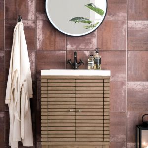 A modern bathroom with a Linden 24 inch Bathroom Vanity in Whitewashed Walnut, brown tiled walls, and a round mirror above its wooden slats. A robe hangs on the wall, soap dispensers rest on the vanity, and a lantern sits beside this chic centerpiece.
