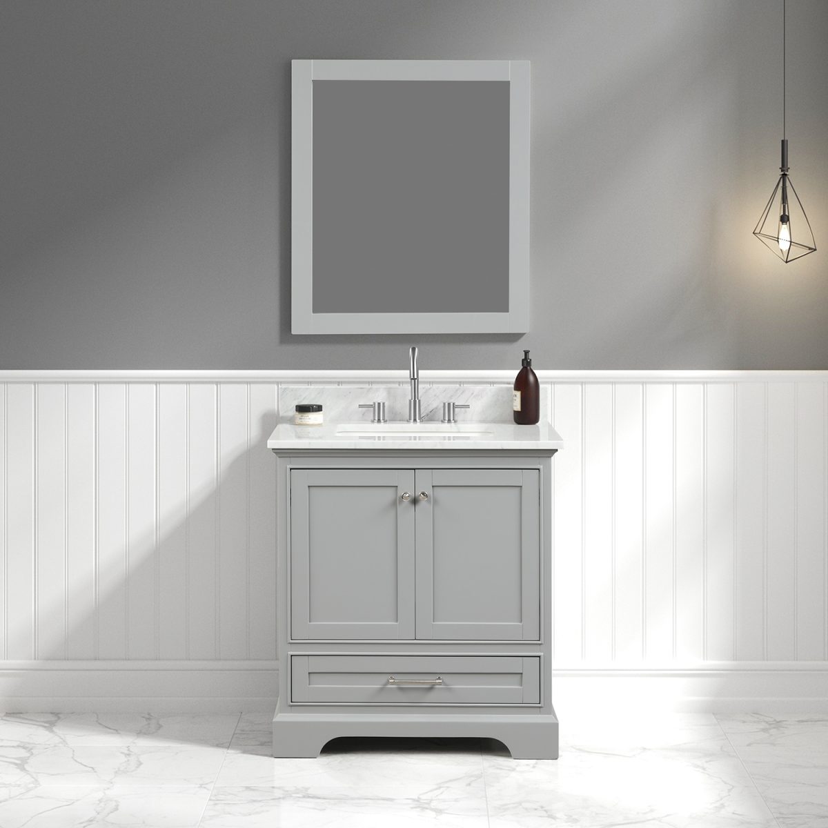 A modern bathroom features a Copenhagen 30 metal gray vanity with a White Carrara marble top and silver faucet, paired with a large rectangular mirror. The walls exhibit white wainscoting and gray paint, while a geometric pendant light on the right complements the marble floor.