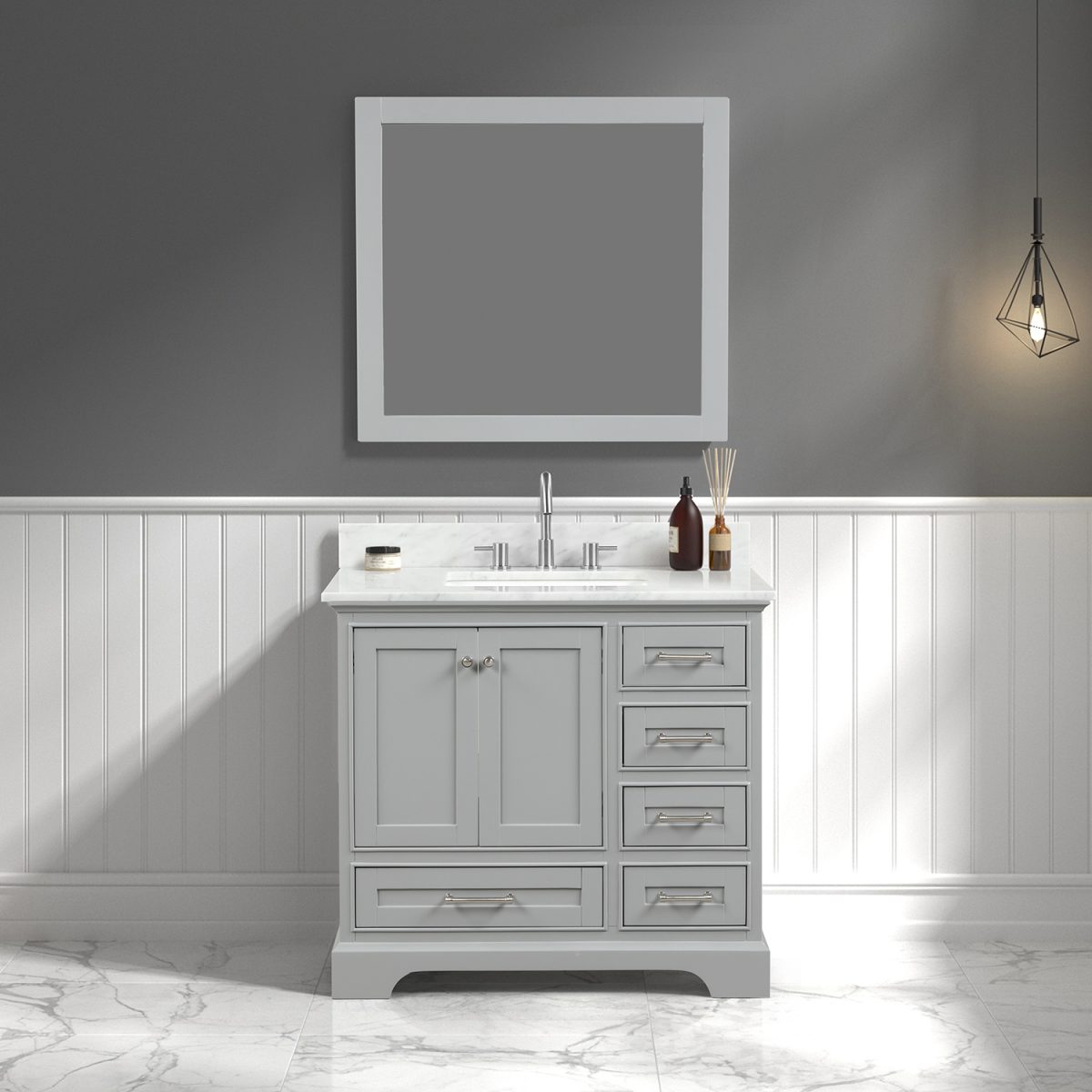 A modern bathroom showcases a white vanity with a marble countertop, silver faucet, decor items, and a large mirror above the Copenhagen 36 inch Bathroom Vanity in Metal Gray with Carrara Marble Top. The walls feature gray and white paneling with a geometric light fixture to the right.