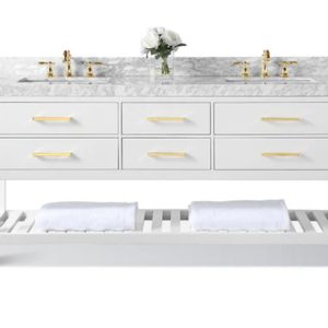 The Elizabeth 72 in. Bath Vanity Set in White features a double sink with six gold-handled drawers, a marble countertop, two gold faucets, and an open lower shelf with folded white towels. A vase of white flowers is placed between the sinks.