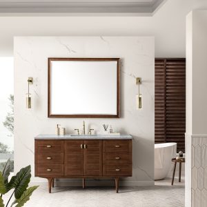 Modern bathroom with an Amberly 60 Single Vanity in Mid-Century Walnut and Carrara Marble Top. A large mirror is flanked by two pendant lights, a freestanding bathtub is in the background, a plant in the foreground, and neutral tones with a partial window view complete the scene.