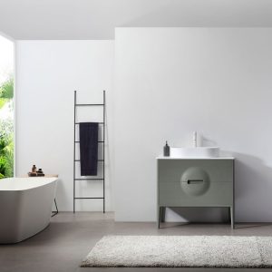 Minimalist bathroom with a freestanding white bathtub, black towel ladder holding a dark towel, Colmar 36 inch Olive Green Freestanding Bathroom Vanity with round detail, and a white rug on a gray floor; bright natural light enters from the left.