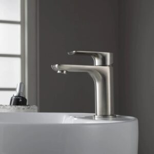 The Austin Single Handle Bathroom Vanity Sink Faucet in brushed nickel is mounted on a white sink, with a blurred bottle and window in the background, creating a clean and minimalist atmosphere.