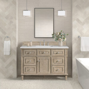 Gorgeous bathroom with a light wood Lorelai 48 inch Vanity Cabinet featuring multiple drawers and a white countertop. Above, a rectangular mirror is flanked by two pendant lights, with a floral vase on the counter. Tiled walls and a towel bar complete the look.