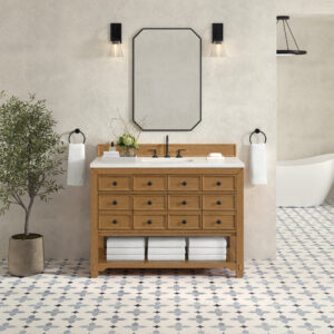 The bathroom features a Malibu 48 inch Bathroom Vanity Cabinet in Amber Birch, accented by a rectangular mirror and two black wall sconces overhead. White towels hang on either side, while a potted plant decorates the tiled floor near the freestanding bathtub.