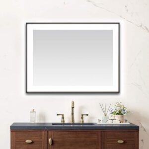 A modern bathroom vanity with a dark countertop, brass faucet, soap dispenser, and small flower arrangement sits beneath the Lexington 48 inch x 36 inch LED Lighted Slim Frame Mirror on a white marble wall.