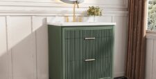 A modern bathroom features the Aveline 30 Inch Freestanding Bathroom Vanity With Top in green with gold hardware, a white countertop, a round backlit mirror, gold wall sconces, black-and-white checkered floor tiles, and a small plant on the counter.