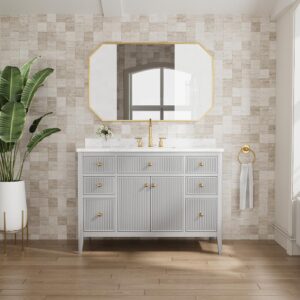 A modern bathroom features the Aveline 48 Inch Freestanding Bathroom Vanity with Top in light gray and gold hardware beneath a large geometric mirror. A potted plant stands to the left, with a towel ring and window on the right.