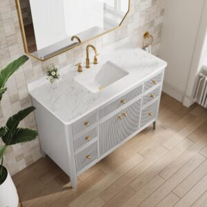 The Aveline 48 Inch Freestanding Bathroom Vanity With Top features a marble countertop, gold faucet and handles, and a small vase of flowers, set against beige tiled walls with a large mirror and a green plant nearby.