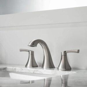 The Vermont 8 Inch Widespread Bathroom Sink Faucet in brushed nickel showcases a curved spout and dual handles on a white marble countertop, set against a light gray wall with a mirror backdrop.